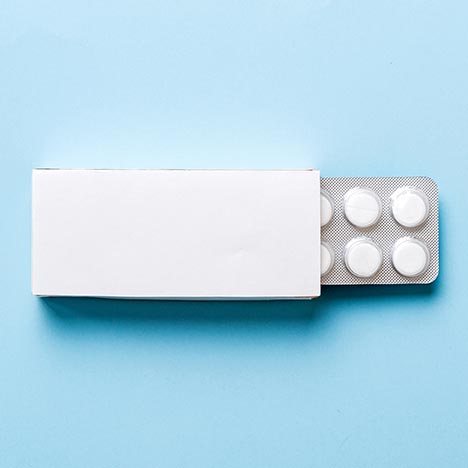 Boîte blanche rectangulaire ouverte sur un fond bleu, laissant apparaître une plaquette de comprimés ronds partiellement sortie.